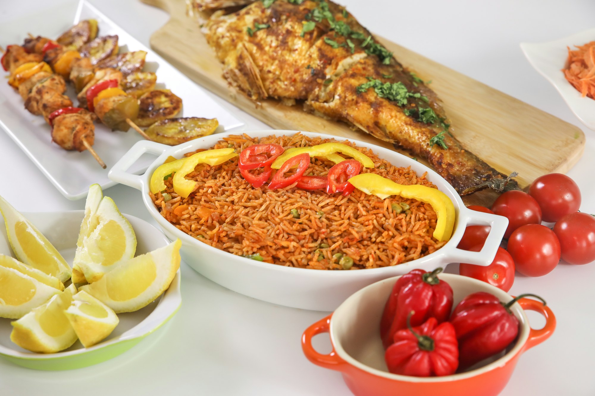 Riz jollof servi avec poisson grillé, brochettes et légumes frais